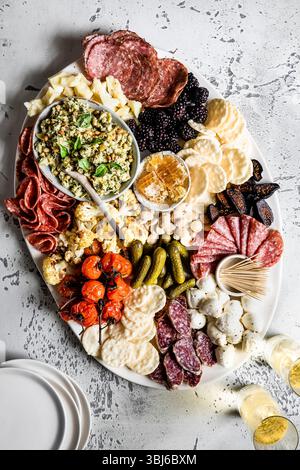 Un elegante tagliere di salumi con una varietà di carni, formaggi, frutta e cracker, accompagnati da bicchieri di vino bianco. Foto Stock