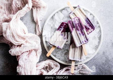 Un piatto di papaveri viola e bianchi poggiati sul ghiaccio, circondato da un tessuto rosa chiaro. Foto Stock