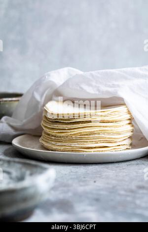 Una pila di tortillas crude su un piatto bianco, parzialmente ricoperto da un panno bianco. Foto Stock