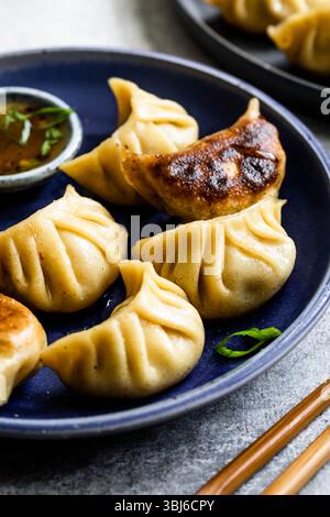 Un piatto di gnocchi cotti al vapore e saltati in padella servito con salsa da immersione su un piatto blu. Foto Stock
