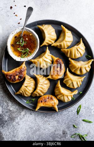 Un piatto di gnocchi fritti servito con una ciotola di salsa e guarniti con cipolle verdi. Foto Stock
