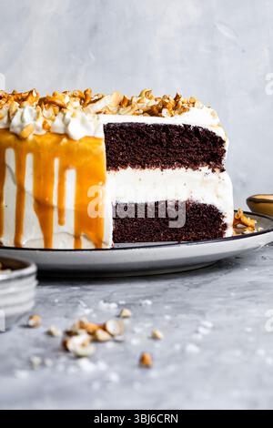 Una torta al cioccolato a fette con glassa bianca e filetto di caramello, ricoperta di noci tritate. Foto Stock