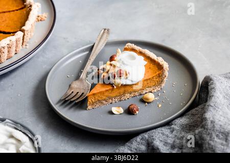 Una fetta di torta di zucca con panna montata e noci su un piatto grigio con una forchetta. Foto Stock