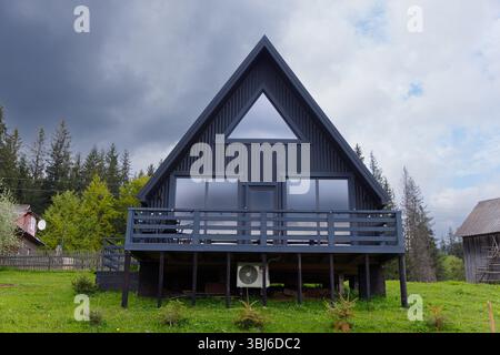 Questa splendida casa con cornice Ad A presenta grandi finestre ed un elegante esterno nero, adagiato su un incantevole sfondo forestale, sfoggia un design moderno Foto Stock