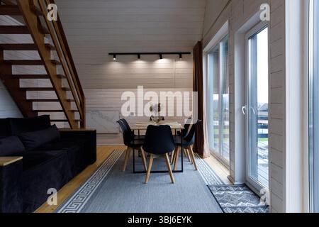 Questo affascinante interno presenta una calda scala in legno, mobili eleganti e un'invitante zona pranzo, che crea uno splendido spazio per il relax e il relax Foto Stock