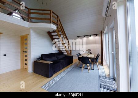 Questa immagine mostra un interno in legno splendidamente progettato con un'atmosfera invitante, caratterizzato da una scala, un morbido divano, una zona pranzo, e. Foto Stock