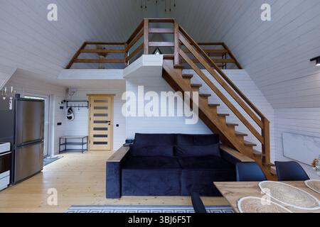 L'immagine mostra un invitante abitacolo in legno con un loft, un comodo divano e una zona pranzo. Legno chiaro e un decor elegante creano un ambiente caldo e accogliente Foto Stock