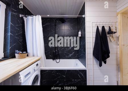 Bagno dal design elegante e moderno con vasca, zona doccia, elegante arredo D con piastrelle in marmo nero e un'atmosfera accogliente Foto Stock