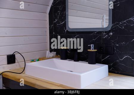 Questa immagine presenta un moderno lavandino da bagno dal design elegante, accessori neri e rustica struttura in legno, creando un'atmosfera elegante Foto Stock