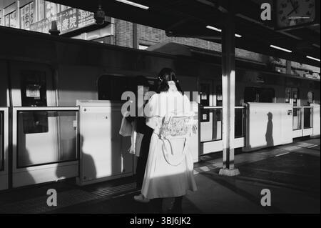 Due donne aspettano alla piattaforma di un treno di Tokyo, il sole getta lunghe silhouette in bianco e nero Foto Stock