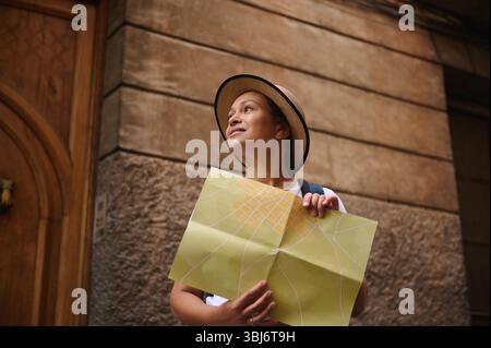 Donna turistica con una mappa che esplora le affascinanti strade di una città vecchia, godendoti i dintorni storici e un senso di scoperta. Foto Stock