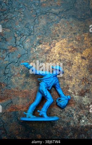 Un cowboy blu brillante si trova saldamente su una superficie robusta, con una mano sollevata con una pistola, mentre l'altra tiene una borsa. Foto Stock