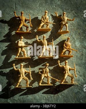 I soldati giocattolo di plastica sono esposti in diverse pose d'azione su una superficie strutturata, gettando ombre che ne evidenziano le forme. Foto Stock