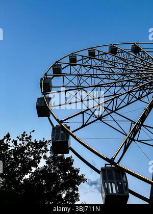 Silhouette della ruota panoramica del carnevale scattata dal basso, con energia dinamica. Perfetto per manifesti di festival, annunci di eventi funebri e immagini di stile di vita gioioso. Foto Stock