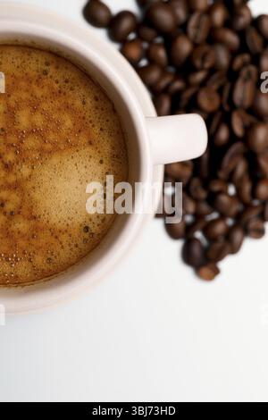 Primo piano di una tazza di espresso appena preparato con chicchi di caffè, che offre un aroma e un sapore ricchi Foto Stock