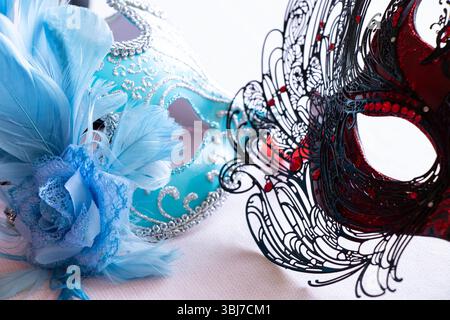 Maschere di carnevale blu chiaro e rosso nero con piume blu e nere su sfondo rosa chiaro, accessorio decorativo Foto Stock