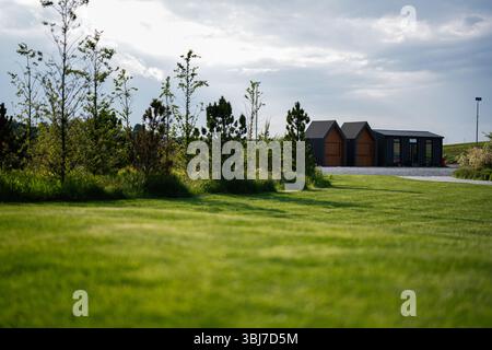 Cabine contemporanee in un lussureggiante prato verde circondato da alberi sullo sfondo nuvoloso Foto Stock