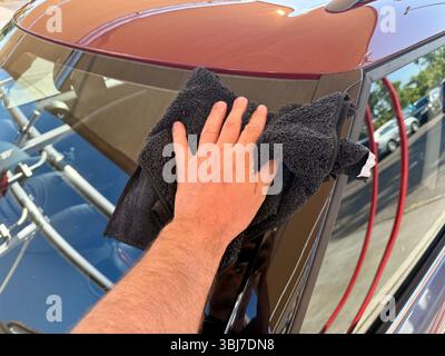 Uomo che pulisce l'auto a mano con un panno in microfibra nero presso il punto di autolavaggio Foto Stock