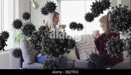 Seduti due donne che tengono tazze con maschera sotto mento e parlano in salotto, sovrapposizioni di virus Foto Stock