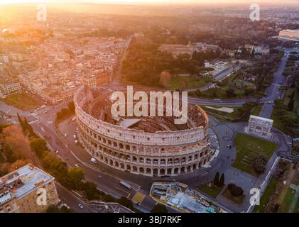 Vista aerea del Colosseo a Roma, in Italia, completamente visibile ad angolo durante l'alba, con un cielo arancione che emette una calda luce mattutina. Foto Stock