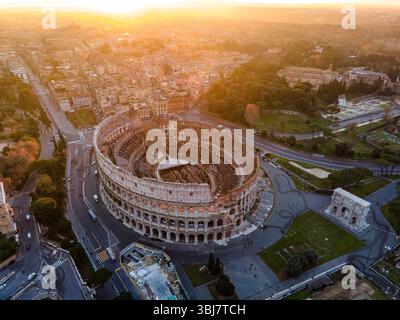 Vista aerea del Colosseo a Roma, in Italia, completamente visibile ad angolo durante l'alba, con un cielo arancione che emette una calda luce mattutina. Foto Stock