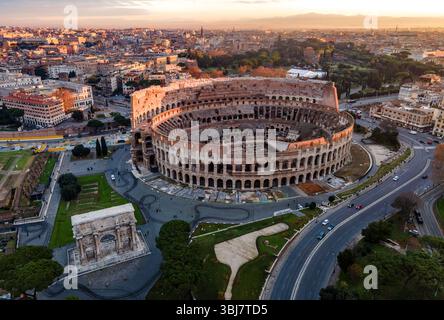 Vista aerea del Colosseo a Roma, in Italia, completamente visibile ad angolo durante l'alba, con un cielo arancione che emette una calda luce mattutina. Foto Stock