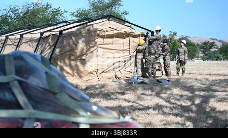 Un Airman del 23rd Combat Communications Squadron si erge su una sedia per regolare la cinghia di una tenda di comunicazione, mentre altri Airmen forniscono supporto da terra, mentre l'ufficiale incaricato ispeziona durante uno schieramento simulato per l'esercitazione NEXUS RISING 25-01 alla Travis Air Force base, California, 5 giugno 2025. Durante l'esercizio, la tenda estenderà i servizi NIPR (non-Secure Internet Protocol router) per una base aerea di spedizione (XAB). NEXUS RISING 25-01 è un esercizio di preparazione su vasta scala progettato per migliorare la capacità di generare e sostenere la mobilità di combattimento e di depl rapido Foto Stock
