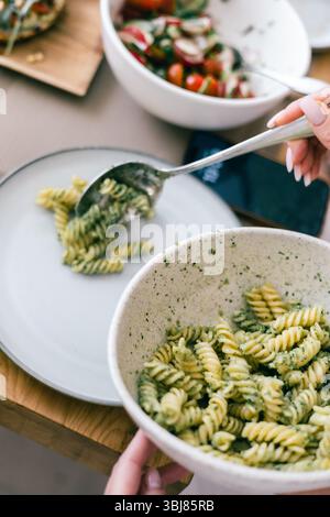Serve pasta con pesto verde fusilli su piatto bianco con insalata sullo sfondo durante il pranzo e la cena Foto Stock