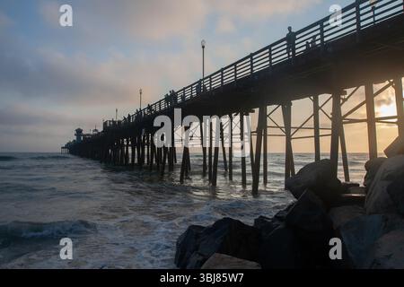 Oceanside Pier al tramonto, San Diego County, California, Stati Uniti, ha modellato le persone sul molo, sul Pacifico e sulle rocce. Foto Stock