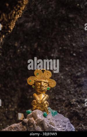 Una squisita figura d'oro precolombiana adornata con smeraldi, esposta su una roccia minerale, che mostra l'arte delle antiche culture colombiane. Foto Stock