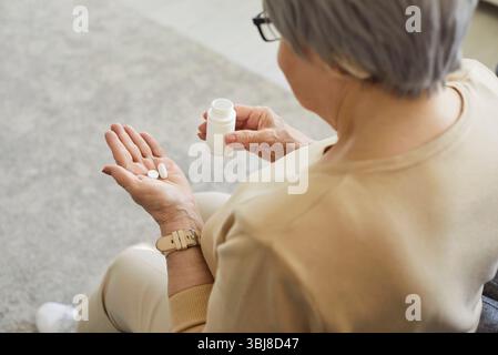 Vista posteriore della donna di mezza età che tiene in mano una bottiglia di farmaci, assumendo la medicina prescritta dal medico Foto Stock