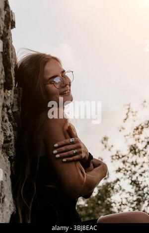 Donna che indossa occhiali Ritratto sorriso all'aperto - Una donna che indossa gli occhiali sorride mentre si appoggia contro una parete all'aperto. Foto Stock