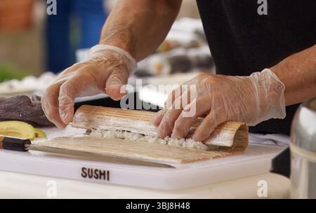 Primo piano dello chef che utilizza un tappetino di bambù mentre prepara i sushi panini freschi su un tagliere. Foto Stock