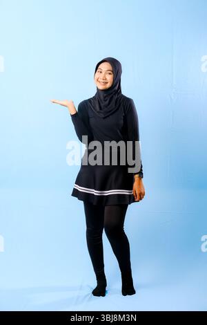Una donna che indossa una gonna nera e pantaloni neri. Sta sorridendo e tenendo la mano in alto Foto Stock