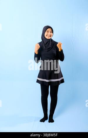 Una donna con una gonna nera e pantaloni neri è in piedi di fronte a un muro blu Foto Stock