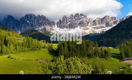 I maestosi monti del Geislergruppe, parzialmente innevati, si innalzano sopra valli e boschi verdeggianti nei pressi di Santa Magdalena, Dolomiti, Foto Stock