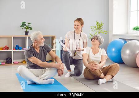 Medico o formatore che parla con la coppia senior durante la sessione di riabilitazione Foto Stock
