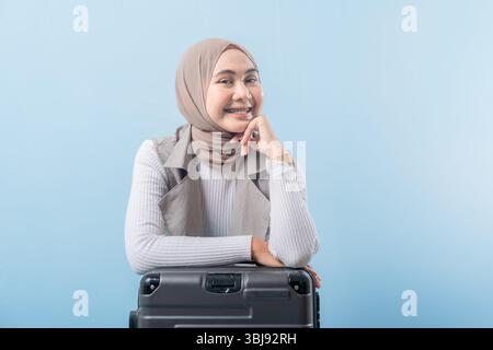 Una donna che indossa una sciarpa per la testa si siede su una valigia. Sta sorridendo e guardando la telecamera Foto Stock