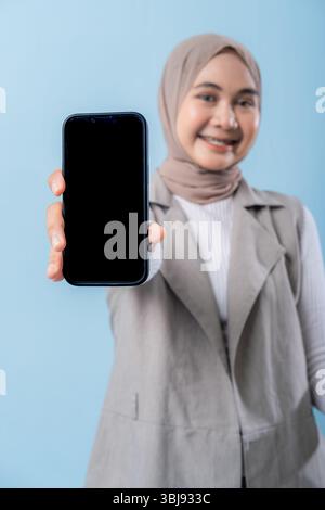 Una donna tiene in mano un cellulare nero e lo indica. Lei sorride ed è felice Foto Stock