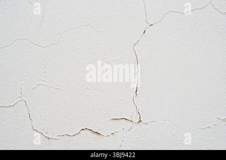 Primo piano di una parete dipinta di bianco con crepe visibili e intonaco che rivela la consistenza e l'usura. Foto Stock