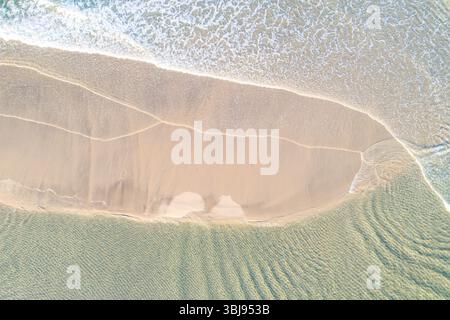 ripresa con drone che cattura gli intricati motivi di schiuma bianca su una costa incontaminata, immagine aerea dall'alto verso il basso dal drone Foto Stock