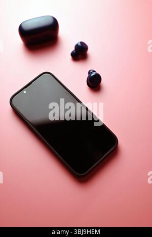 smartphone spento con cuffie wireless su sfondo rosa Foto Stock