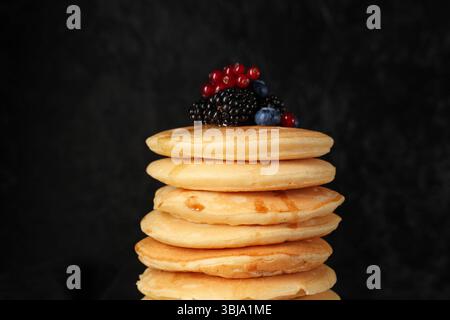 Frittelle dolci con diversi frutti di bosco freschi su sfondo nero, primo piano Foto Stock
