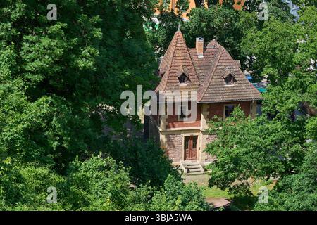 Storica casa in mattoni rossi circondata da lussureggianti alberi verdi in Germania. Affascinante architettura di un vecchio edificio in un tranquillo giardino o foresta. Foto Stock