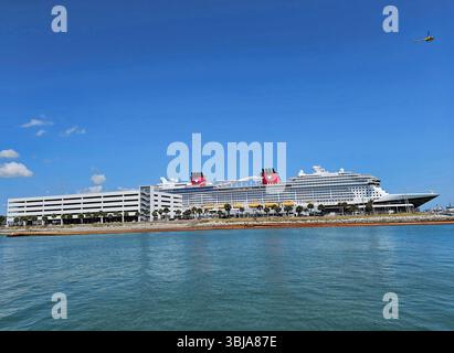 Nave da crociera Disney a Port Canaveral, Florida. La nave è più alta del parcheggio a 6 piani. Un elicottero giallo brillante vola sopra la testa. Foto Stock
