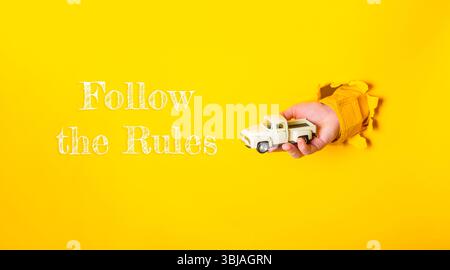 La mano che tiene in mano un carrello giocattolo viene mostrata con le parole seguire le regole scritte sotto di esso. Concetto di responsabilità e rispetto delle linee guida Foto Stock