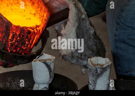 Il metallo fuso dal crogiolo si riversa nello stampo ceramico durante la fusione del bronzo nel processo di cera persa. Foto Stock