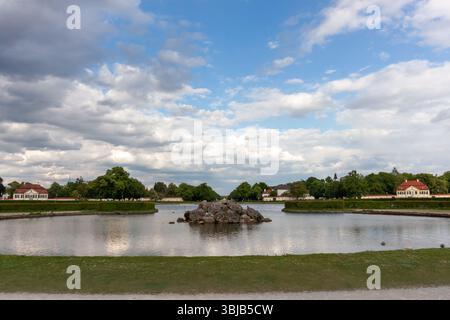 Una vista panoramica grandangolare dei tranquilli canali del Castello di Nymphenburg a Monaco, Germania, sotto un bel cielo con un mix di macchie blu e drammatico Foto Stock