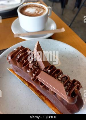 Elegante pasticceria al cioccolato con strati di mousse e scaglie di cioccolato decorativi serviti con una tazza di caffè su un tavolo da caffè Foto Stock