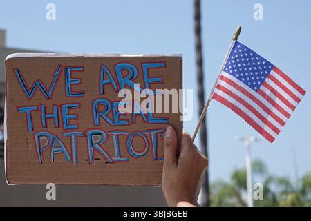 Los Angeles, CA, USA - 14 giugno 2025: Un cartello fatto a mano con la scritta WE ARE THE REAL PATRIOTS viene mostrato accanto a una bandiera americana in un rally "No Kings". Foto Stock